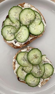 two pieces of bread with cucumbers on them sitting on a plate next to each other