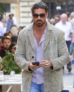 a man with sunglasses and a beard is looking at his cell phone while walking down the street