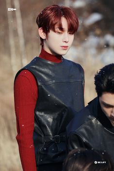 a man with red hair wearing a black leather vest and standing next to another person