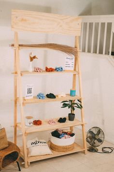 a wooden shelf with baskets and clothes on it in front of a stair case next to a fan