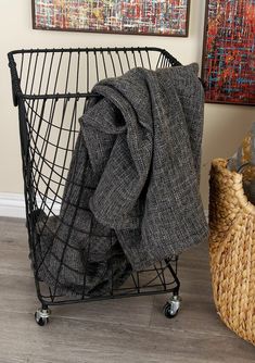 a black wire basket with a blanket on it next to a painting and wicker basket