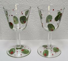 two wine glasses with green leaves and red berries on them, sitting side by side