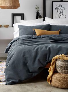 a bed with grey sheets and pillows in a bedroom next to a potted plant