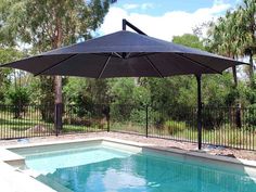 an outdoor pool with a black umbrella over it and trees in the backgroud