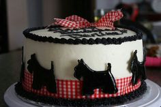 a cake decorated with black dogs and red gingham ribbon on top of a table