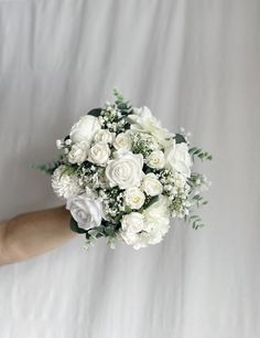 a bouquet of white flowers is held by someone's hand on a white sheet