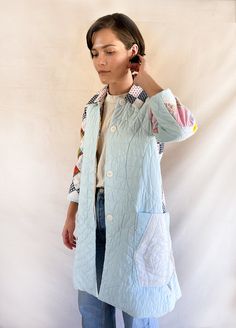 a woman standing in front of a white backdrop wearing a blue jacket with patches on it