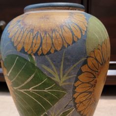 a large vase with flowers painted on it's sides and leaves around the edges