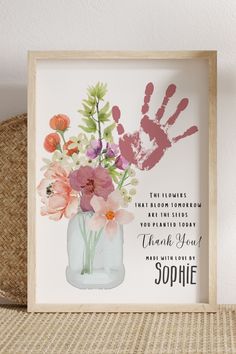 a vase with flowers in it sitting on top of a table next to a handprint