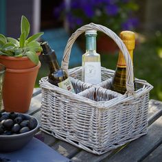 two bottles of wine in a wicker basket on a picnic table with olives