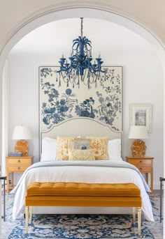 a white bed sitting under a blue chandelier