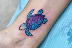 a small turtle tattoo on the wrist and hand is blue, purple, and pink