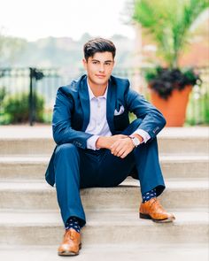 a man in a blue suit sitting on steps with his legs crossed and wearing brown shoes