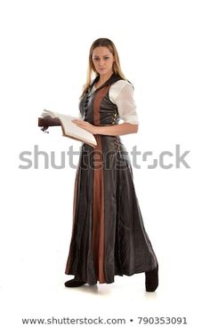 a woman dressed in medieval clothing is holding a book and looking at the camera while standing on