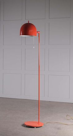 an orange floor lamp with a red shade on it's base and a white wall in the background