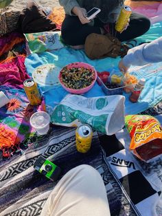 a person sitting on a blanket with food and drinks in front of them at the beach