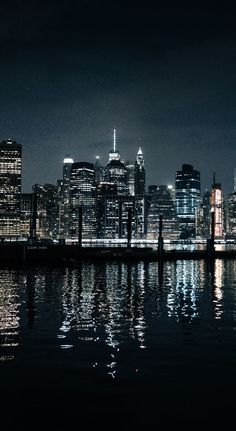 the city is lit up at night with lights reflecting in the water and dark clouds