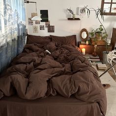 an unmade bed with brown sheets in a bedroom next to a window and potted plants