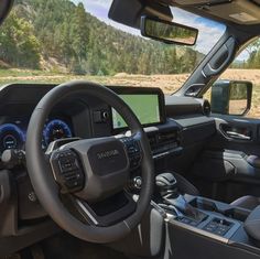 the interior of a truck with dashboard, steering wheel and dash board on display in front of mountains