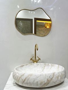 a marble sink in front of a mirror with gold faucet and two mirrors above it