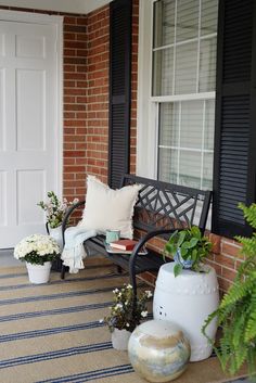 a bench sitting on top of a porch next to a white vase filled with flowers