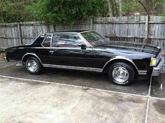 a black car parked in a driveway next to a wooden fence