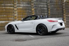 a white bmw z4 roadster parked in front of a stone wall with black rims