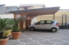 a small car parked in front of a wooden covered parking lot with potted plants