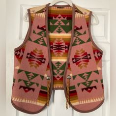 a pink sweater vest hanging on a white door with an arrow pattern and tassels