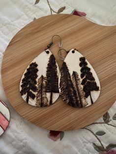 wooden earrings with black and white designs on them sitting on a wood board next to a flowery tablecloth