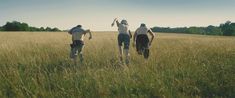 three people running through tall grass in a field