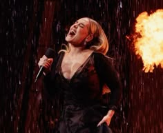 a woman singing into a microphone in front of a fireball with her mouth open