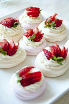 small cupcakes with whipped cream and strawberries on top are sitting on a white platter