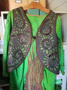 a green and brown shirt with an intricate design on the chest, hanging from a wooden hanger