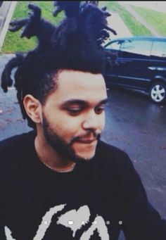 a man with dreadlocks on his head is sitting in front of a car