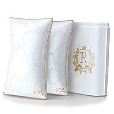 two white pillows with gold trim on them next to a case for the letter r