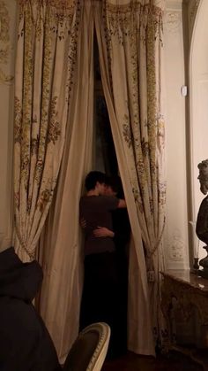 a man and woman standing in front of a window next to a statue on a table