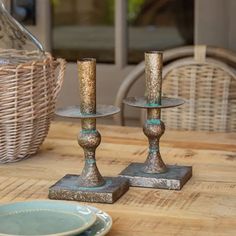 two metal candlesticks sitting on top of a wooden table next to plates and baskets