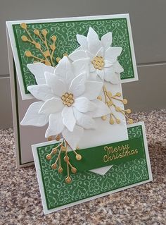 a christmas card with white flowers and green trimmings on the front, sitting on a granite countertop