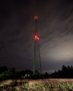 a tall tower sitting in the middle of a field at night with red lights on it