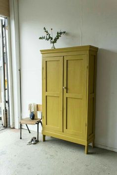 a yellow cabinet sitting in the corner of a room next to a chair and plant