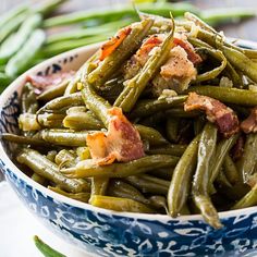 a bowl filled with green beans and bacon on top of a table next to other vegetables