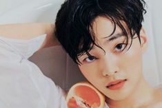 a young man holding a grapefruit in front of his face while taking a bath