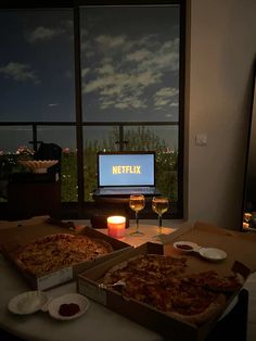 two pizzas sitting on top of a table next to wine glasses and a tv