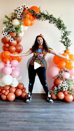 a woman is standing in front of balloons and flowers with her arms spread out to the side