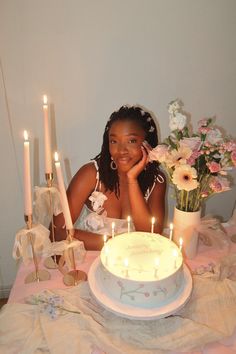 a woman sitting in front of a cake with lit candles on the table next to it