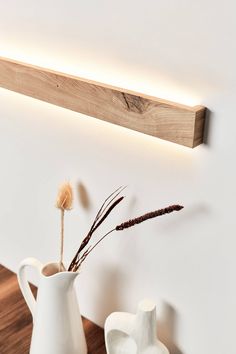 a white vase with some dried flowers in it next to a wooden shelf on the wall