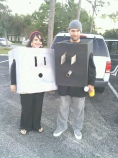 a man and woman standing in a parking lot holding cardboard cutouts with faces on them