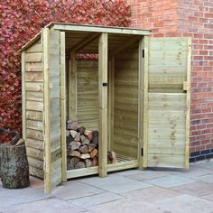 a wooden shed sitting next to a pile of firewood in front of a brick wall