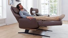 a man laying on top of a recliner chair in a living room next to a window